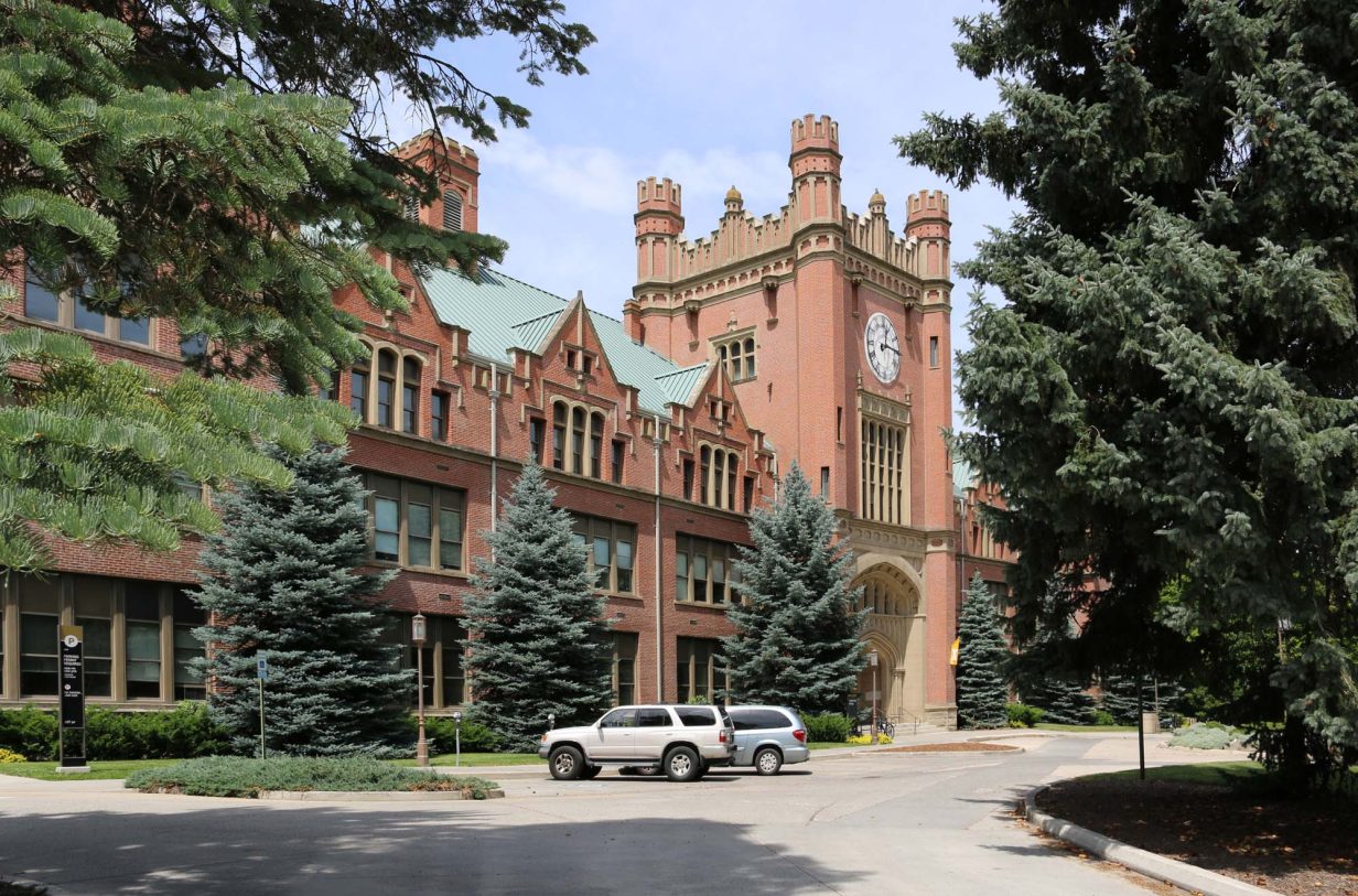 A picture of the University of Idaho's administration building. It's a red brick building with a castle-like structure surrounded by evergreen trees.